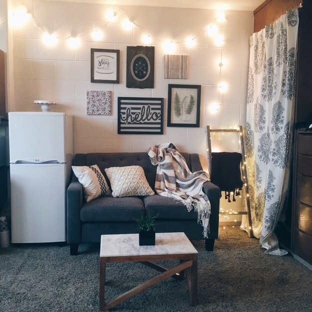 A room with a blue-gray color scheme, with a small refrigerator, love seat, small table, and posters