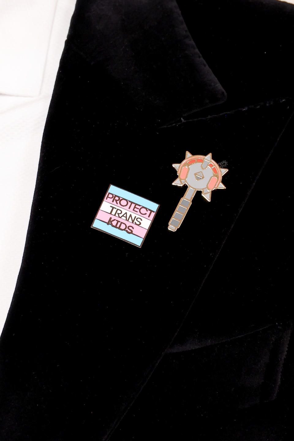 Two lapel pins on a jacket, one with text "PROTECT TRANS KIDS," and the other shaped like a key