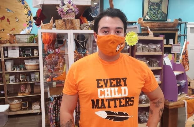 Wyler Diome-Montour displays a shirt that is available for sale at The Purple Dragonfly Trading Post in Kahnawake, where the store is thanking customers for supporting Indigenous initiatives. (Kwabena Oduro/CBC - image credit)