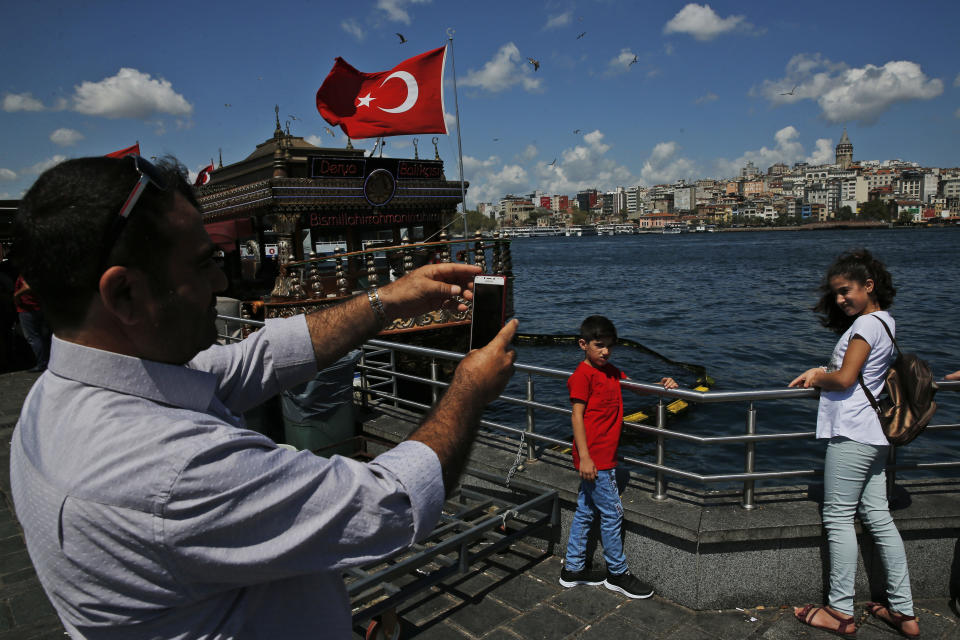 In this Monday, Aug. 20, 2018 photo, tourists take pictures by the Golden Horn, leading to the Bosporus Strait, in Istanbul. Tourists have returned in droves to Turkey, helped this summer by the sharp fall in the value of the Turkish lira following economic uncertainty and a rift with the United States.(AP Photo/Lefteris Pitarakis)