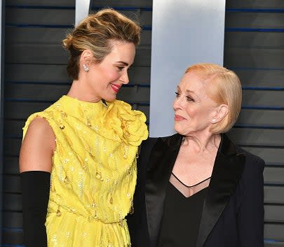 Sarah Paulson in an embellished dress with black gloves, and Holland Taylor in a black suit, smile at each other at a formal event