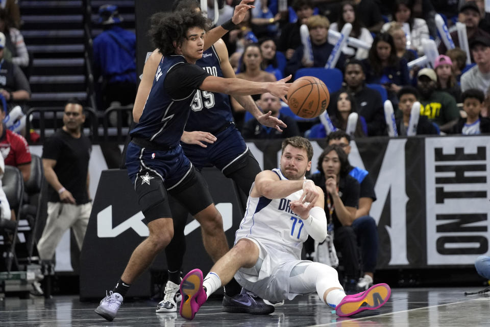 Dallas Mavericks guard Luka Doncic (77) passes the ball past Orlando Magic guard Anthony Black, front left, as he falls backward during the second half of an NBA basketball game, Monday, Nov. 6, 2023, in Orlando, Fla. (AP Photo/John Raoux)