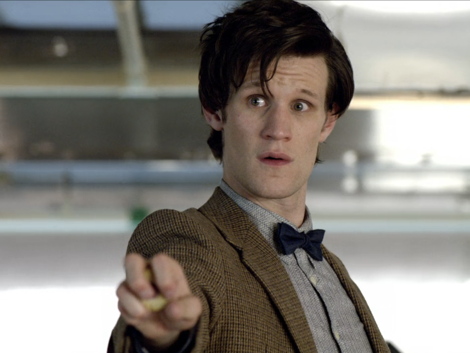 Matt Smith as the Eleventh Doctor from Doctor Who, pointing with intense expression. He is wearing a tweed jacket, bow tie, and light-colored shirt