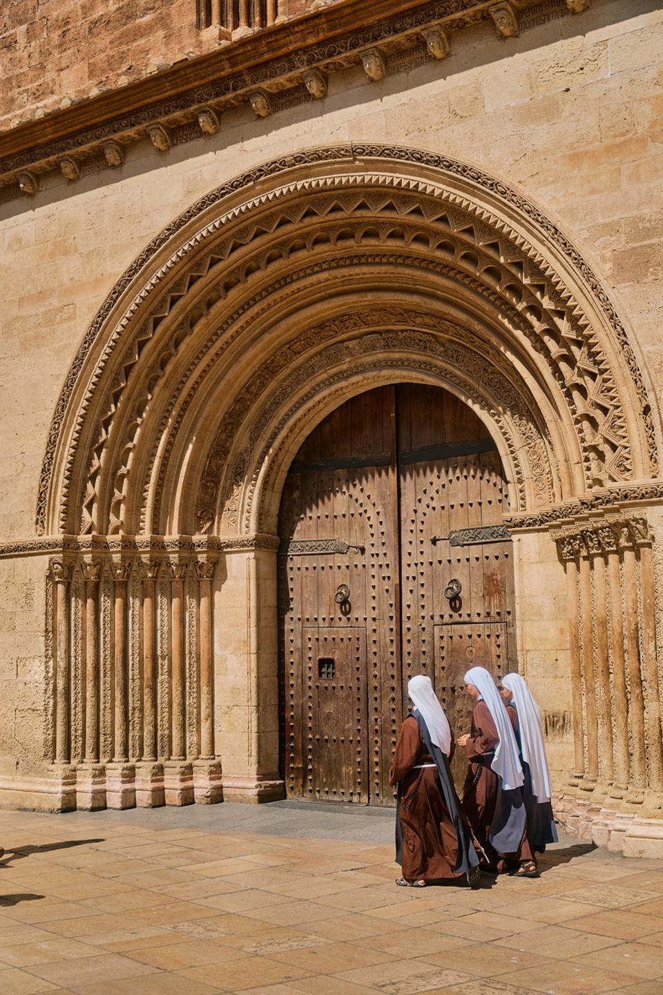 Nuns walking past the exterior entrance to a cathedral