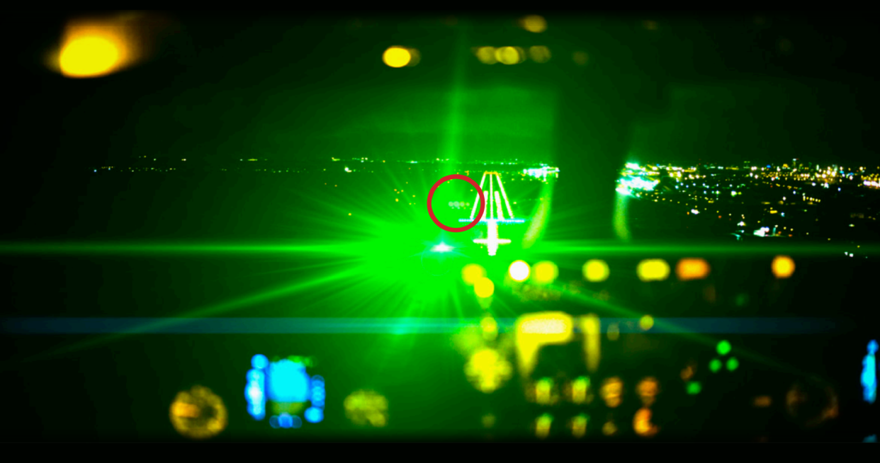 Image shows laser strike illumination in a flight simulator from a pilot's perspective on a landing approach.