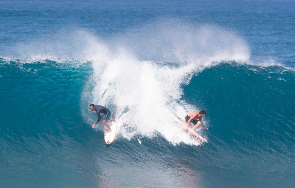 Hawaii's pro surfers Bruce Irons (R) and Eli Olson (L) ride a wave during the Vans World Cup of Surfing at Backdoor Pipeline on the north shore of Oahu on November 27, 2019.