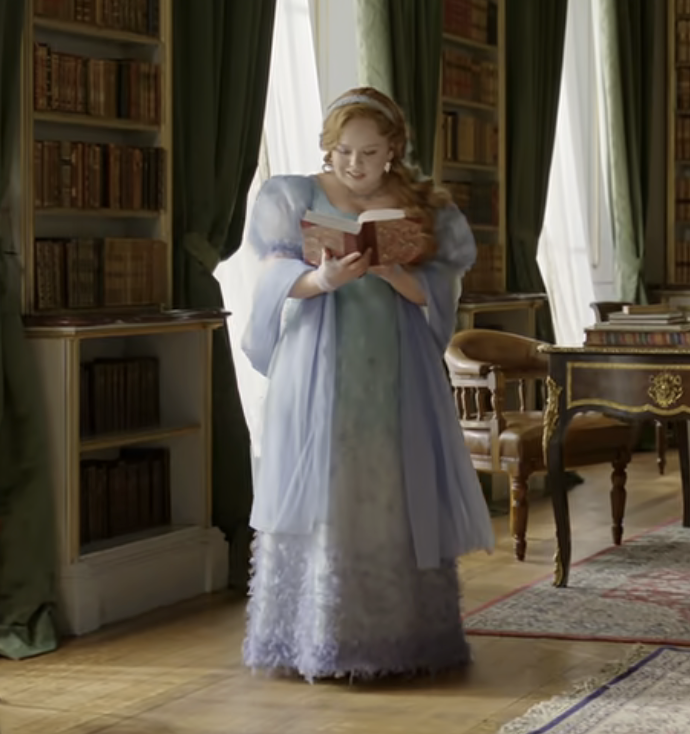Penelope in a period-style gown with ruffles and feathery accents, reading a book in a room filled with bookshelves and classic wooden furniture