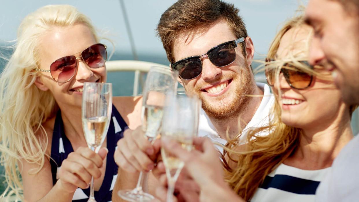 vacation, travel, sea, friendship and people concept - smiling friends with glasses of champagne on yacht.