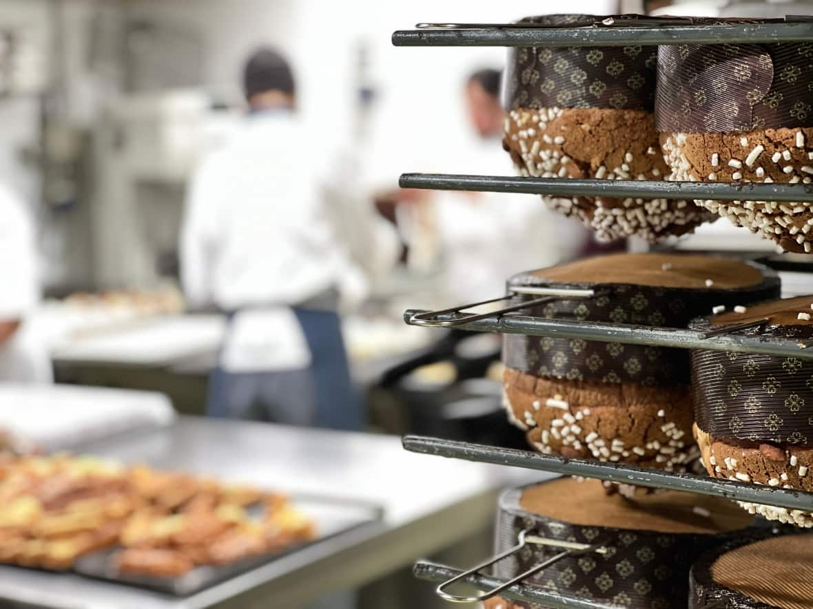 Panettone sweet breads, these ones the Turin version, are hung upside down to cool as pastry chefs work in the background. These days, many chefs are using ingredients like chocolate, cherries and nuts, but Italian chefs warn that any recipe that strays from the classic is not technically a panettone. (Megan Williams/CBC - image credit)