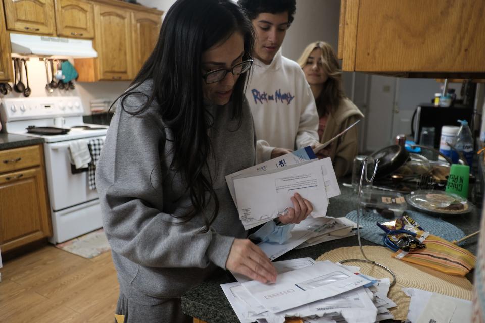 A woman goes through her mail, while two teenagers stand to her side.