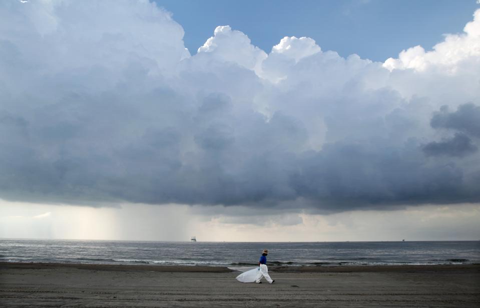 FILE - A worker leaves the beach as storm clouds approach in Grand Isle, La., May 30, 2010. When a deadly explosion destroyed BP's Deepwater Horizon drilling rig in the Gulf of Mexico, tens of thousands of ordinary people were hired to help clean up the environmental devastation. These workers were exposed to crude oil and the chemical dispersant Corexit while picking up tar balls along the shoreline, laying booms from fishing boats to soak up slicks and rescuing oil-covered birds. (AP Photo/Jae C. Hong, File)