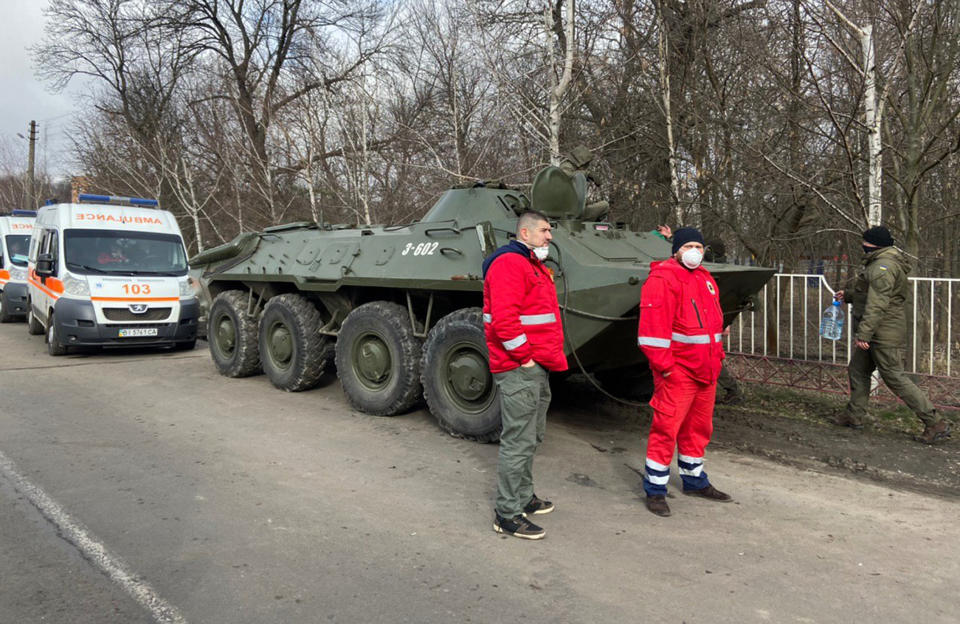 Medics stand next tp Ukrainian police gathing to block protesters who planned to stop busses with passengers from the Ukrainian aircraft chartered by the Ukrainian government for evacuation from the Chinese city of Wuhan, outside Novi Sarzhany village, Ukraine, Thursday, Feb. 20, 2020. Several hundred residents in Ukraine's Poltava region protested to stop officials from quarantining the evacuees in their village because they feared becoming infected. Demonstrators put up road blocks and burned tires, while Ukrainian media reported that there were clashes with police, and more than 10 people were detained. (AP Photo)