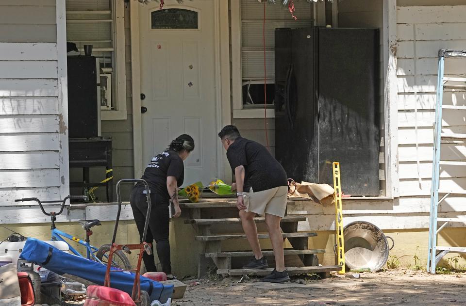 Two people place flowers on the porch of a home.