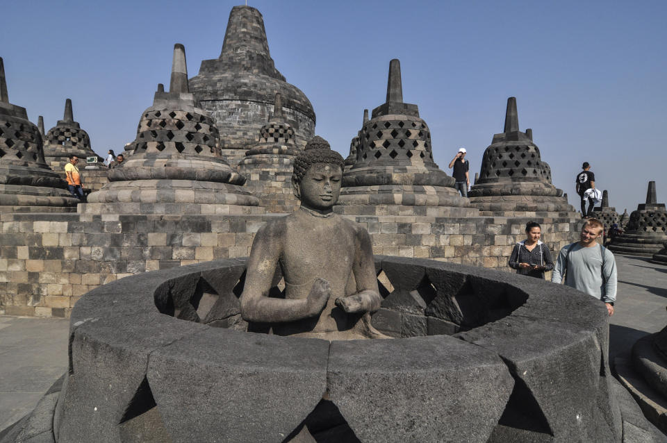In this Monday, Aug. 12, 2019, photo, tourists inspect a Buddha statue at Borobudur Temple in Magelang, Central Java, Indonesia. The Indonesian city of Yogyakarta and its hinterland are packed with tourist attractions, including Buddhist and Hindu temples of World Heritage. Yet many tourists still bypass the congested city and head to the relaxing beaches of Bali. Recently re-elected President Joko Widodo wants to change this dynamic by pushing ahead with creating "10 new Balis," an ambitious plan to boost tourism and diversify South Asia's largest economy. (AP Photo/Slamet Riyadi)