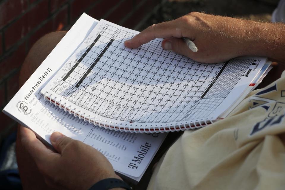 A fan keeps track of the box scores during a Cape Cod League baseball game between the Chatham Anglers and the Bourne Braves, Wednesday, July 12, 2023, in Bourne, Mass. For 100 years, the Cape Cod League has given top college players the opportunity to hone their skills and show off for scouts while facing other top talent from around the country. (AP Photo/Michael Dwyer)
