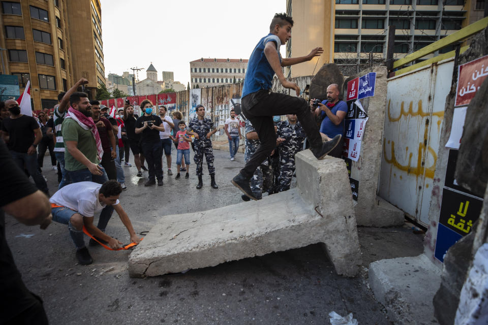 Anti-government protesters remove a concrete wall that was installed by security forces to prevent them from reaching the government palace in Beirut, Lebanon, Thursday, July 2, 2020. Major retailers in Lebanon announced Thursday they will temporarily close in the face of an increasingly volatile currency market and their inability to set prices while the local currency tumbles before the dollar. (AP Photo/Hassan Ammar)