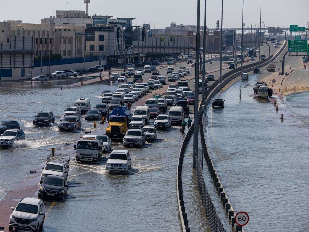 Vehicles drive through standing floodwater caused by heavy rain in Dubai, United Arab Emirates, Thursday, April 18, 2024. It was the heaviest rain the desert nation has ever recorded, a deluge that flooded out Dubai International Airport and disrupted flights and left four people dead in the UAE.  (Christopher Pike/Associated Press - image credit)