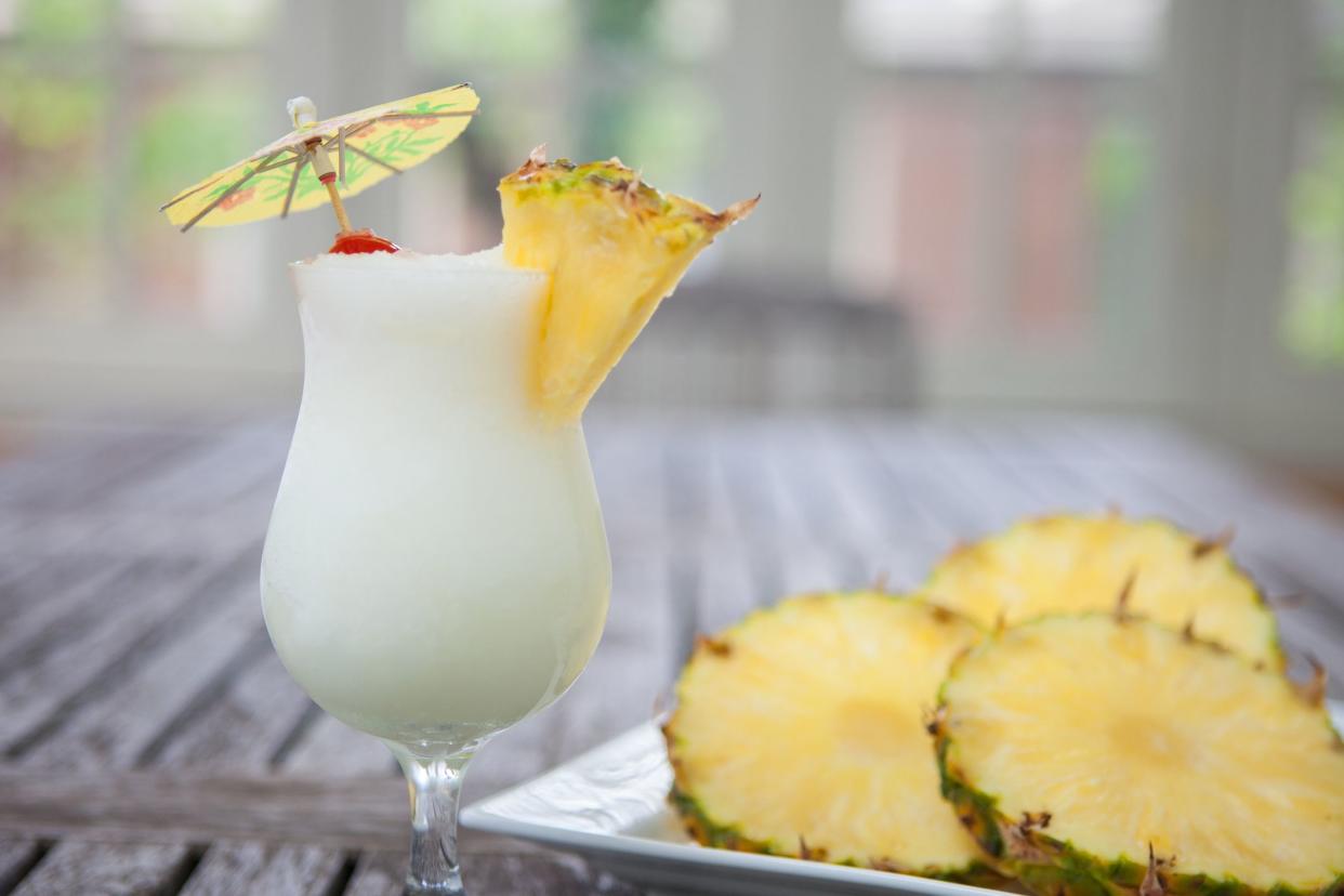 piña colada next to pineapple slices on plate on wooden table