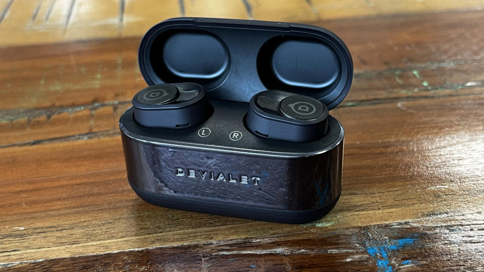 The Devialet Gemini II wireless earbuds shown on a textured wooden background