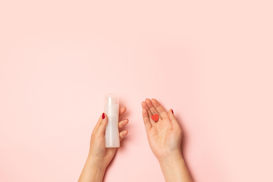 Selling love concept. Womens hands hold intimate grease and a red heart shape on a pink background