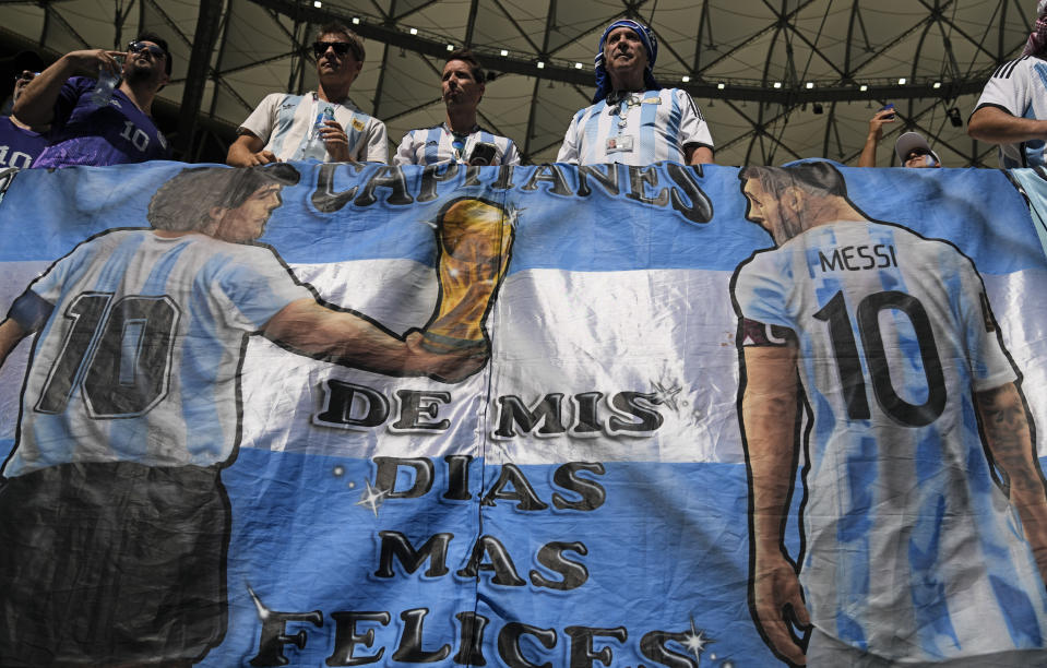 Argentina's fans hold a banner showing Diego Maradona handing over the trophy to Lionel Messi prior to the World Cup group C soccer match between Argentina and Saudi Arabia at the Lusail Stadium in Lusail, Qatar, Tuesday, Nov. 22, 2022. (AP Photo/Natacha Pisarenko)