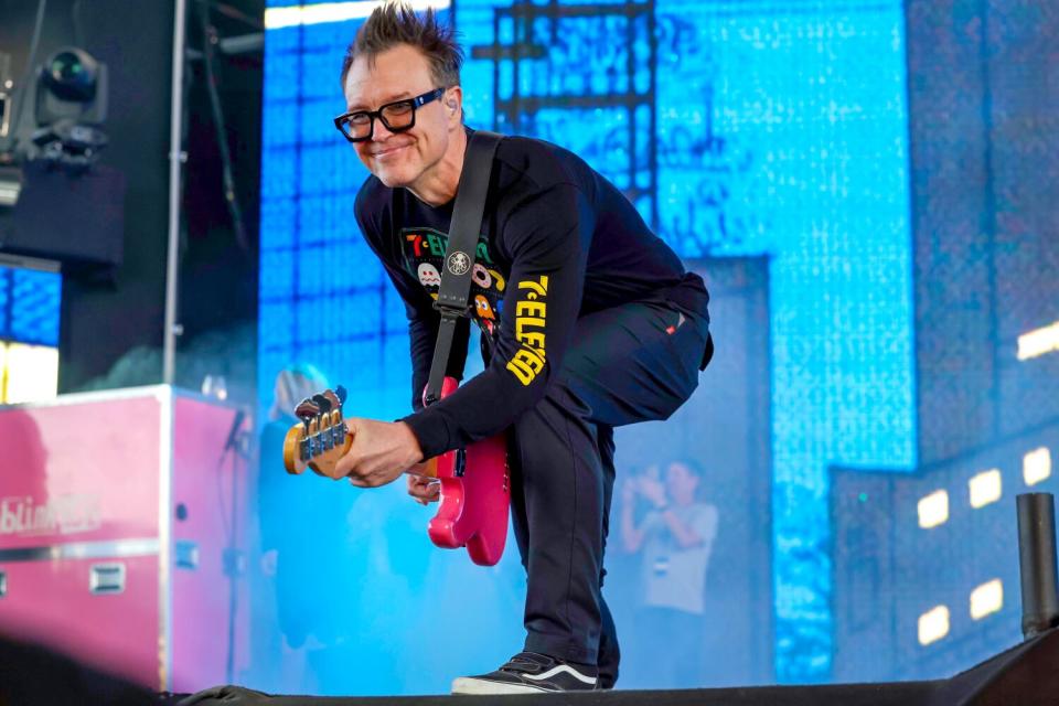 A smiling man leans down and plays guitar.