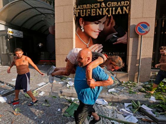 A man carries away an injured girl while walking through debris past in the Achrafiyeh district (AFP via Getty Images)