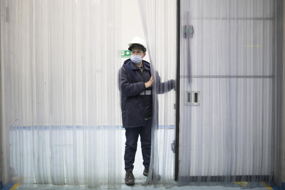 A worker peers through a curtain during a media tour of a site where freezers will store COVID-19 vaccines, during a media tour of a Health Ministry warehouse in Bogota, Colombia, Tuesday, Jan. 19, 2021. (AP Photo/Ivan Valencia)