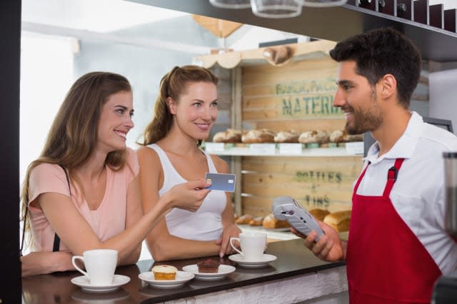 Friends with woman holding out credit card at coffee shop