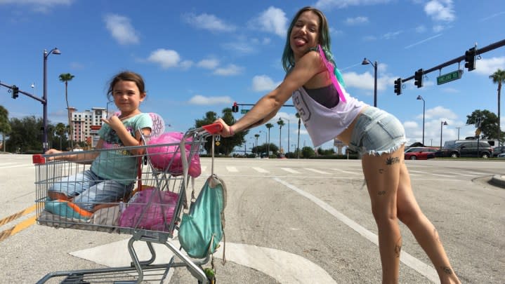 A mother pushes a young girl in a shopping cart.