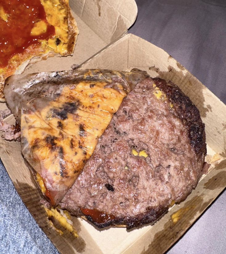 A cardboard box containing a half-eaten burger with a large patty and melted cheese
