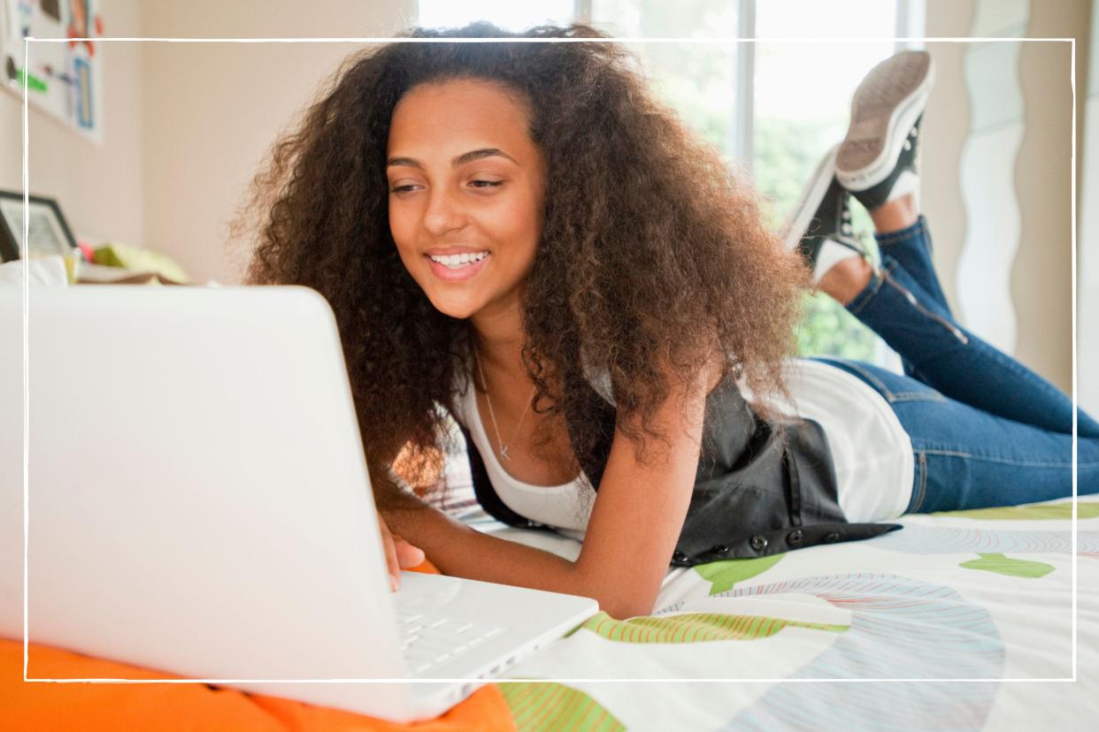  Smiling teen girl lying on her bed looking at her laptop. 