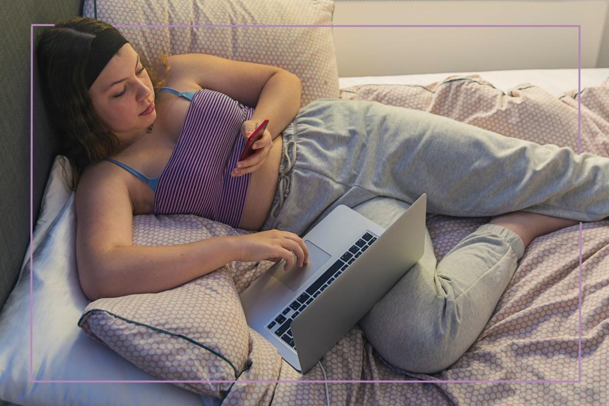  Teen lounging in bed with phone and laptop. 