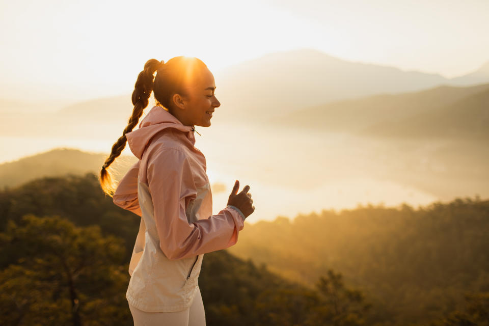 Female athlete jogging by the nature. Happiness and wellbeing, healthy lifestyle with physical activity. Pretty woman laughing when exercising with amazing sunrise view. Harmony with nature.