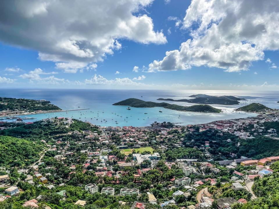 An overhead view of a coastal settlement with brightly-colored buildings and light-blue colored waters and islands off in the distance