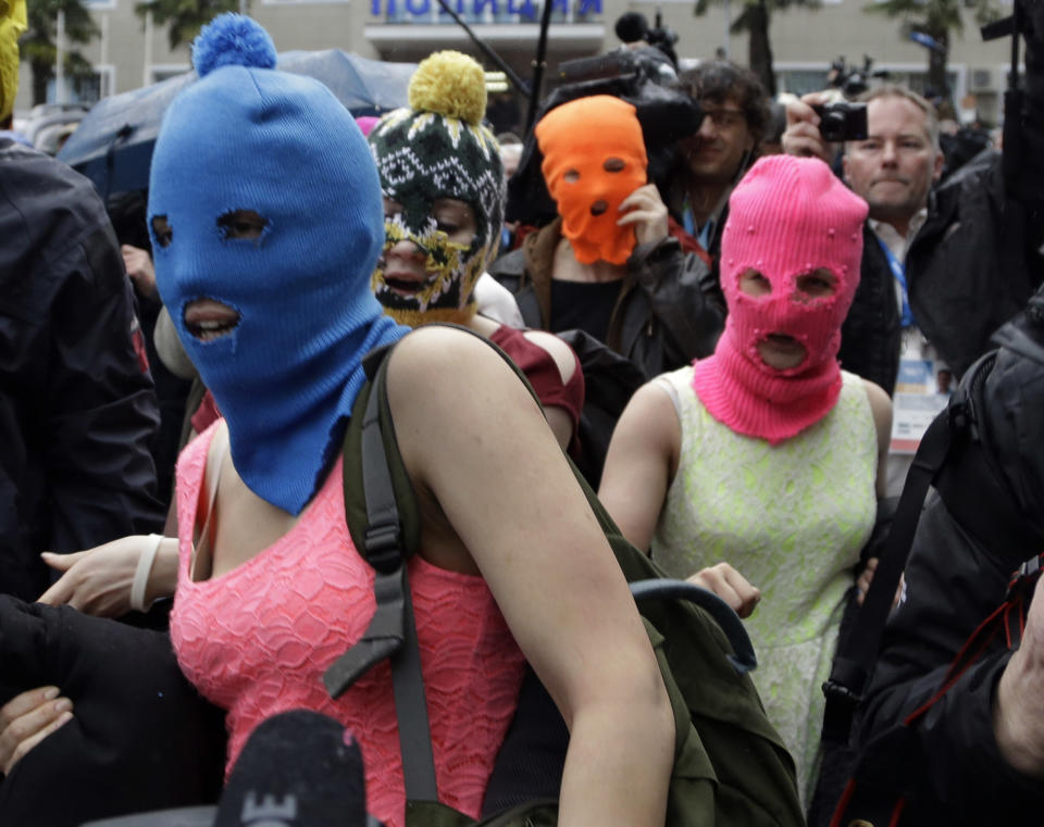 Russian punk group Pussy Riot members Nadezhda Tolokonnikova, in the blue balaclava, and Maria Alekhina, in the pink balaclava, make their way through a crowd after they were released from a police station, Tuesday, Feb. 18, 2014, in Adler, Russia. No charges were filed against Tolokonnikova and Alekhina along with the three others who were detained. (AP Photo/Morry Gash)