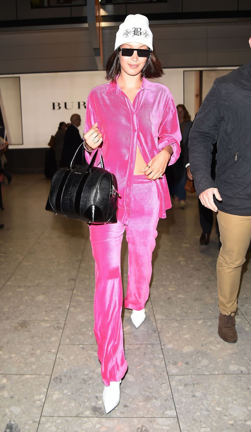 <p>In a hot pink velour suit, Giuseppe Zanotti white booties, white beanie, rectangular sunglasses and black handbag at London's Heathrow Airport.</p>