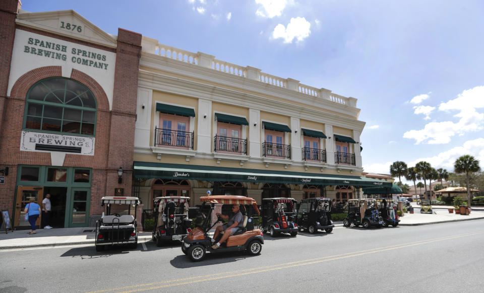 In this Thursday, March 19, 2020 photo, golf carts are lined up outside one of the few open restaurants in The Villages, Fla., as three town squares closed due to the coronavirus through the end of the month. Living in what is perhaps the largest concentration of seniors in the U.S., residents had gone about their busy lives until this week,. (AP Photo/John Raoux)