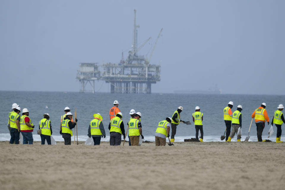 FILE - Workers in protective suits continue to clean the contaminated beach with a platform in the background in Huntington Beach, Calif., on Oct. 11, 2021. A pipeline operator and two subsidiaries have agreed to plead guilty to negligently discharging oil off the Southern California coast in connection with a pipeline break that covered beaches with blobs of crude. (AP Photo/Ringo H.W. Chiu, File)