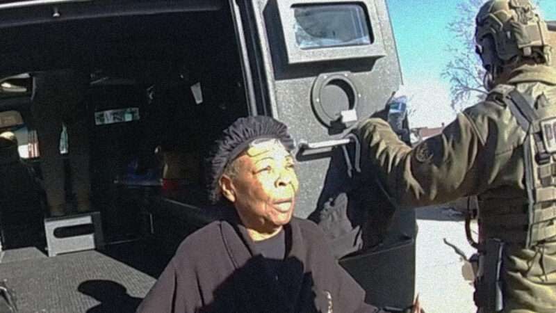 Ruby Johnson sits on the bumper of a vehicle with its back doors open while a man wearing camo holds one door open