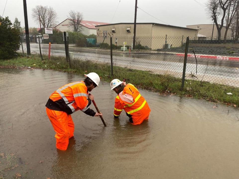 Caltrans workers Kyle Ingle, left, and Zach Westerhuis work to clear a drain next to Highway 101 in Paso Robles as a storm batters San Luis Obispo County on Jan. 9, 2023.