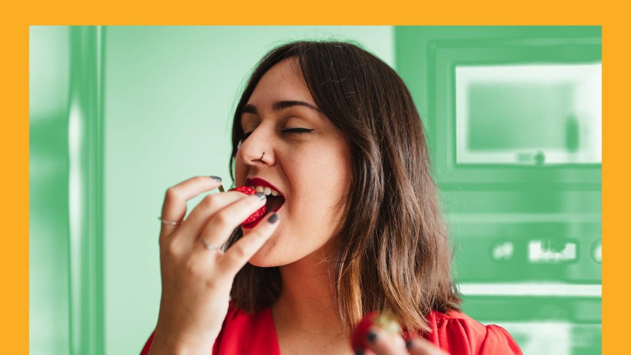 How to Make Mindful Eating a Regular Part of Your Diet , front view of a young woman in red shirt eating a strawberry in the home kitchen