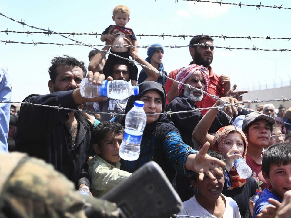 Syrian refugees receive water while they mass at the Turkish border as they flee intense fighting in northern Syria between Kurdish fighters and Islamic State militants in Akcakale, southeastern Turkey, Monday, June 15, 2015.