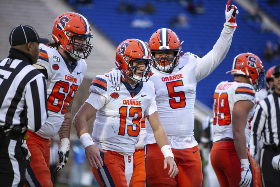 FILE - In this Nov. 16, 2019, file photo, Syracuse's Tommy DeVito (13) celebrates with Chris Elmore (5) and Airon Servais (68) after a play during an NCAA college football game against Duke in Durham, N.C. The Syracuse Orange have missed three practices because of concerns about COVID-19 safety protocols, but the players so far have publicly exhibited a dose of solidarity about playing during the coronavirus pandemic. (AP Photo/Ben McKeown, File)