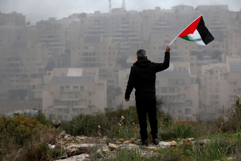 A demonstrator holds a Palestinian flag as the Jewish settlement of Modiin is seen in the background, during a protest in the village of Bilin in the Israeli-occupied West Bank