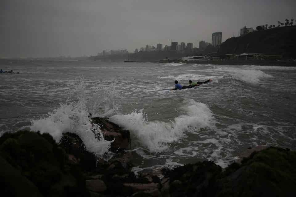 An instructor paddles out with a student during a surf lesson at Barranquito beach in Lima, Peru, Thursday, July 25, 2019. Today, dozens of schools teach locals and tourists from across the world how to ride waves at beaches with Hawaiian names in Lima's Miraflores district, while professional surfers from across the Americas prepare to compete when the sport is featured for the first time in the Pan American Games in the Peruvian capital.(AP Photo/Rebecca Blackwell)