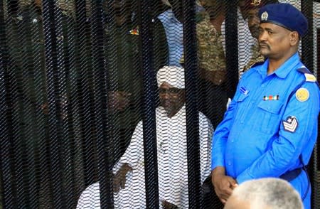 Sudan's former president Omar Hassan al-Bashir sits guarded inside a cage at the courthouse where he is facing corruption charges, in Khartoum