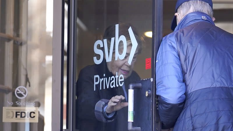 People enter and depart a Silicon Valley Bank branch location through a glass door, in Wellesley, Mass., Monday, March 27, 2023. North Carolina-based First Citizens is to buy Silicon Valley Bank, the tech industry-focused financial institution that collapsed earlier this month.