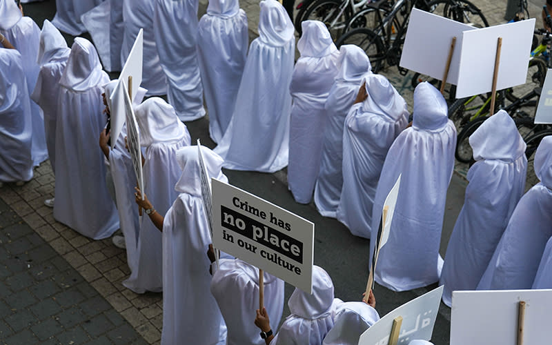 Palestinian citizens of Israel wearing long white robes with hoods protest over the spiraling rate of violent crime. One sign reads "Crime has no place in our culture"