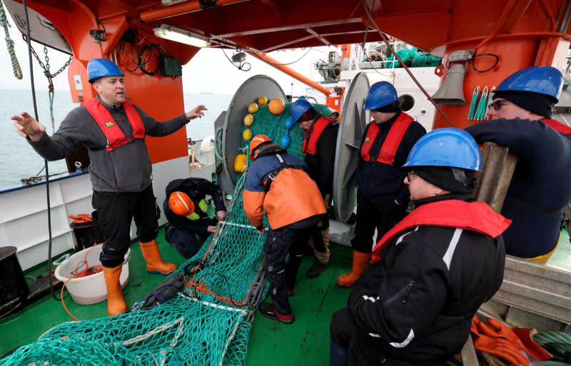 On board the fisheries research vessel Solea in the Baltic Sea, Daniel Stepputtis (l), biologist and fisheries technician at the Thünen Institute of Baltic Sea Fisheries, talks to crew members and fishermen equipping a trawl net with cameras for the next deployment. Bernd Wüstneck/dpa